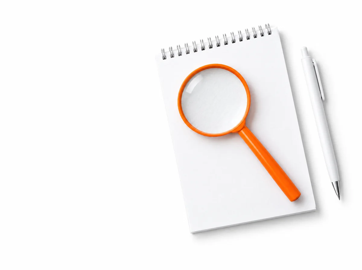 Illustration : une loupe orange posée en travers d'un bloc-notes blanc, un stylo à côté.